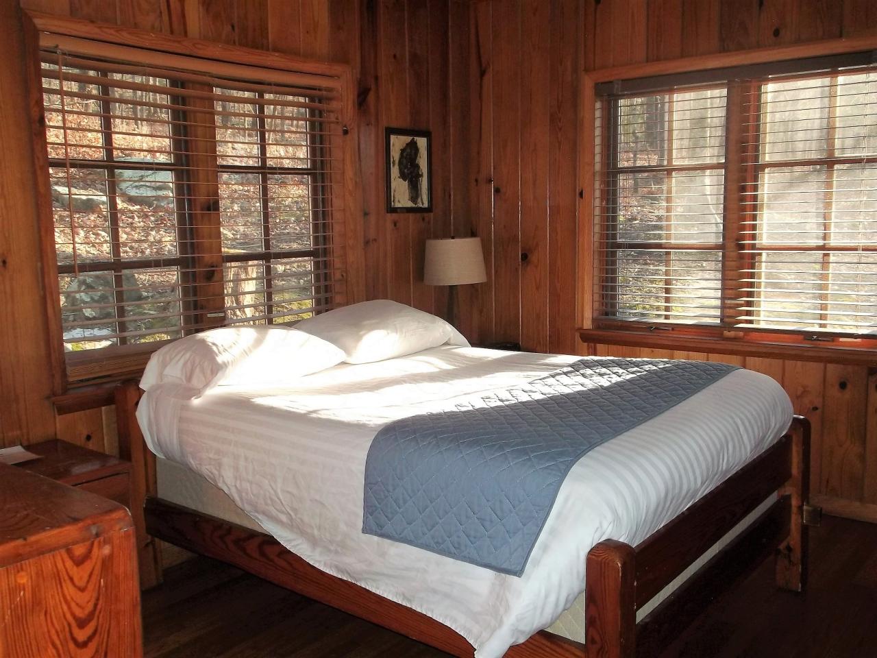 View of one of the bedrooms in Cabin 3 including a bed, dressers and two large windows